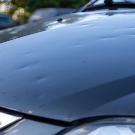 Detailansicht der Motorhaube beim Auto mit Hagelschaden. Es sind alles Dellen von den Hagelkörnern zu sehen.