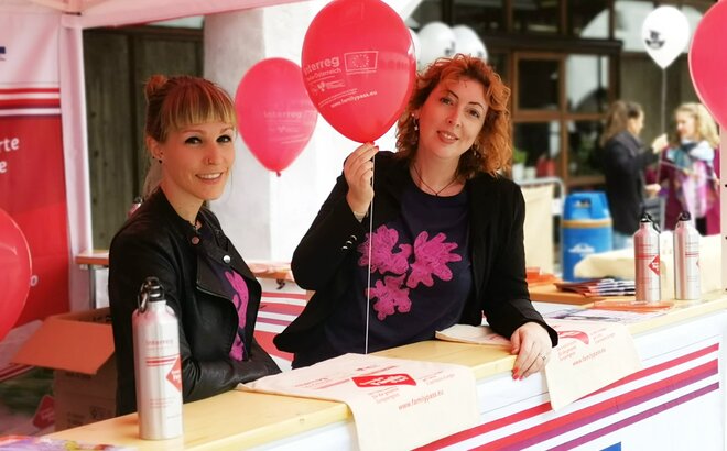 Cora Cavicchi steht mit einer Mitarbeiterin im Faltpavillon bei einer Veranstaltung. In der Hand hält sie einen Luftballon.