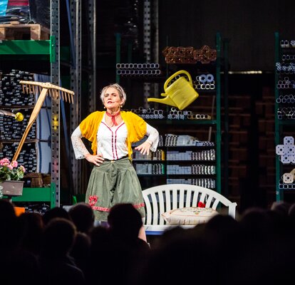 The actress Ingrid Maria Lechner is standing on the stage and performing a drama with different utensils.