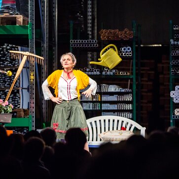 The actress Ingrid Maria Lechner is standing on the stage and performing a drama with different utensils.
