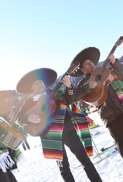 Die Musiker bei den mexikanischen Meisterschaften singen und spielen Gitarre im Schnee. Es strahlt die Sonne.