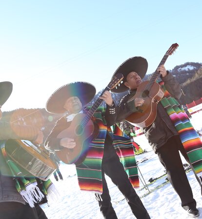 Die Musiker bei den mexikanischen Meisterschaften singen und spielen Gitarre im Schnee. Es strahlt die Sonne.