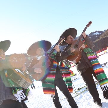 Die Musiker bei den mexikanischen Meisterschaften singen und spielen Gitarre im Schnee. Es strahlt die Sonne.