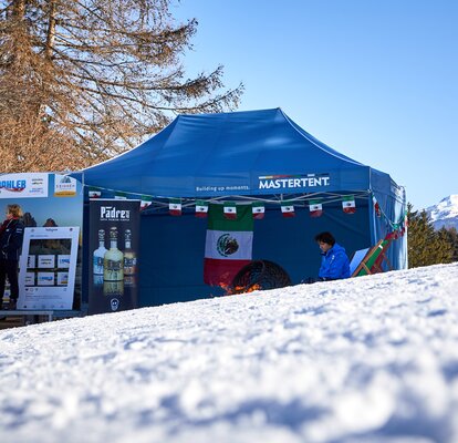 Blauer Faltpavillon steht am Pistenrand eines Skirennens.