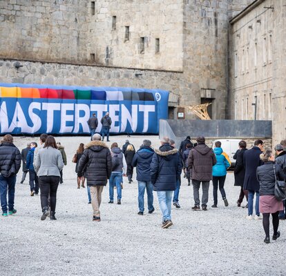 Die Vertreter befinden sich im Gelände der Festung Franzensfeste und gehen auf einen aufblasbaren MASTERTENT Werbeträger zu.