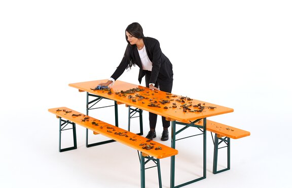 Frau entfernt mit einem blauen Tuch das Laub auf der Bierzeltgarnitur.