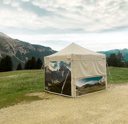 Personalised gazebo. A gazebo from MASTERTENT, printed with pictures of lake Braies. It is located in the green meadow in front of mountains.