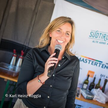 Die Moderatorin von Südtirol kocht, Silvia Fontanive, steht in der mobilen Küche auf einer Wiese. Daneben steht ein großer Kochtopf. | © Karl Heinz Röggla