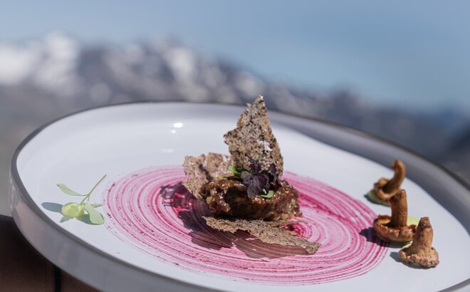 Hauptspeise aus Lamm, Goldbrasse, Urkarotte und Caponata im Rahmen von Südtirol kocht am Schnalstaler Gletscher. Dahinter sieht man das Bergpanorama.