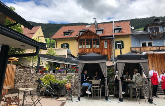 Zwei Lodenzelte von Mastertent stehen auf der Terrasse eines Bistros. Sie dienen als Catering-Zelte. Darunter genießen die Kunden die Getränke.  