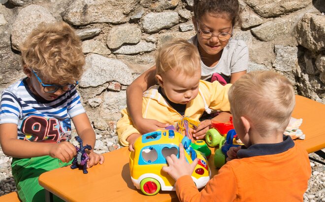 Detailaufnahme der kleinen Bambini-Garnitur mit 4 Kindern, die auf dem Tisch mit Ihrem Spielzeug spielen.
