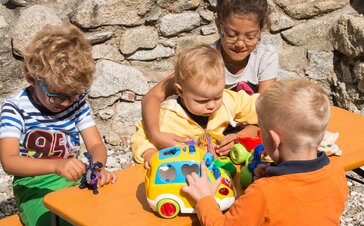 Detailaufnahme der kleinen Bambini-Garnitur mit 4 Kindern, die auf dem Tisch mit Ihrem Spielzeug spielen.