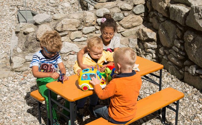 4 Kleinkinder spielen mit ihrem Spielzeug auf der kleinen Bierzeltgarnitur "Bambini".