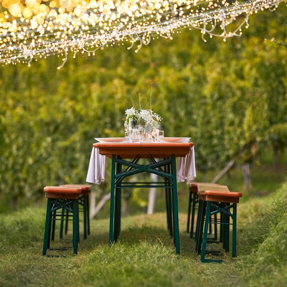 The classic beer tent set is decorated with white-green flower bouquets and stands amidst vines under hanging fairy lights.