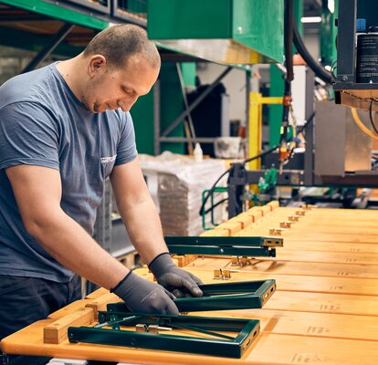 A man is mounting the green underframe to the wooden plate of the beer bench. 