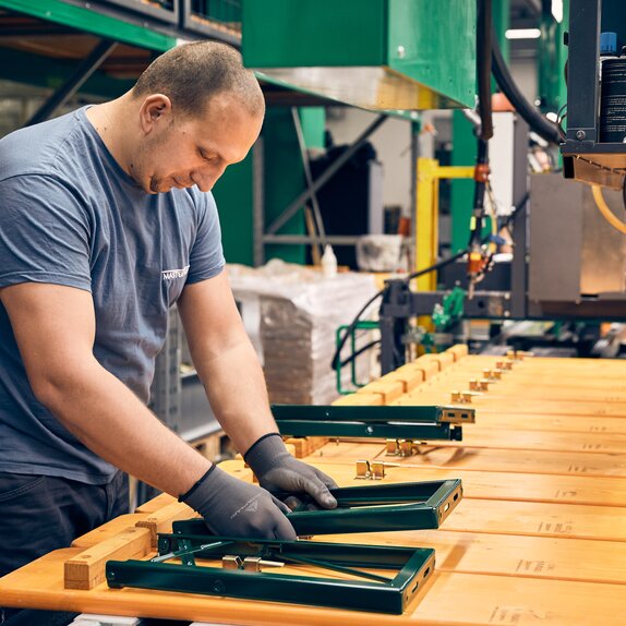 A man is mounting the green underframe to the wooden plate of the beer bench. 