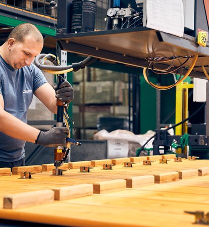 A production employee is assembling the foldable beer benches. 