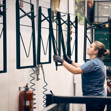 A woman is powder coating the base frames of the classic beer tables.