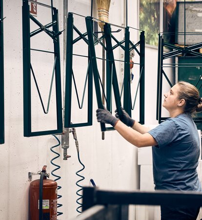 Die Untergestelle der klassischen Biertische werden von einer Frau pulverbeschichtet.