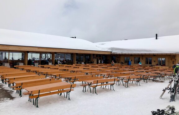 Biertischgarnituren stehen vor der Hütte "Granatalm" im Schnee. Die Biertischgarnituren haben alle eine Lehne.