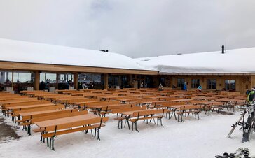 Biertischgarnituren stehen vor der Hütte "Granatalm" im Schnee. Die Biertischgarnituren haben alle eine Lehne.