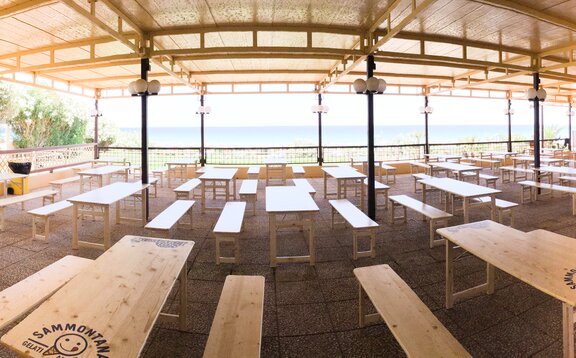 Naturfarbene Rusticagarnituren auf der Terrasse im Lido San Lorenzo. Dahinter sieht man den Strand und das Meer.