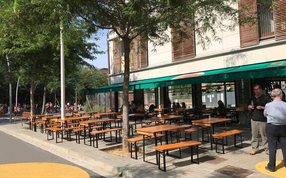 Auf der Terrasse vor dem Restaurant stehen kurze Biertischgarnituren nebeneinander.