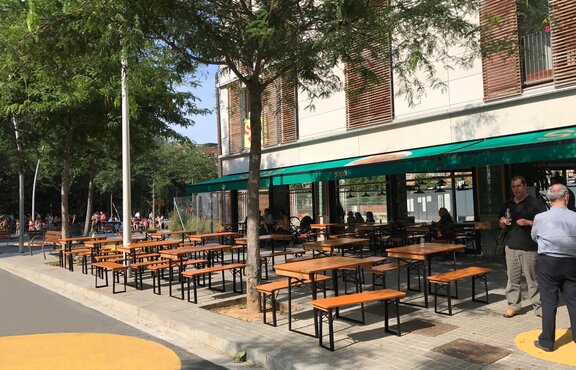 Auf der Terrasse vor dem Restaurant stehen kurze Biertischgarnituren nebeneinander.
