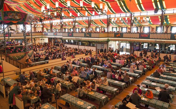 Das Marstall Festzelt auf dem Oktoberfest. Die Tische haben grüne Tischdecken. Die Gäste trinken und feiern im Zelt.