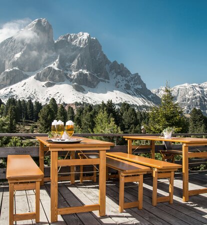 Table and bench set with solid wood base frame on a terrace on  the Würzjoch. Behind it the moutain Peitler Kofel. There are 4 beers on the table. 