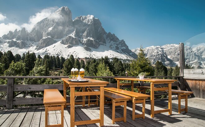 Table and bench set with solid wood base frame on a terrace on  the Würzjoch. Behind it the moutain Peitler Kofel. There are 4 beers on the table. 