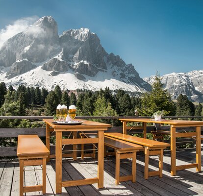 Table and bench set with solid wood base frame on a terrace on  the Würzjoch. Behind it the moutain Peitler Kofel. There are 4 beers on the table. 