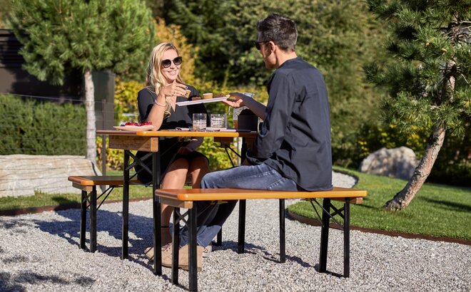 Das Paar sitzt auf der kurzen Bierzeltgarnitur "Shorty" im Garten und isst zu Mittag.