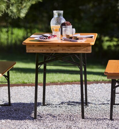 Front view of the Shorty table and bench set. On the short beer tent set are cake desserts and a carafe of orange juice prepared for breakfast. 