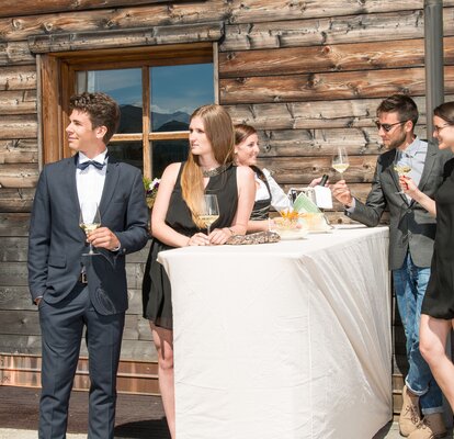 The foldable bar table StandUp is covered with an elegant beige table housing. The waitress is serving drinks to the 4 elegantly dressed guests leaning at the bar table. 
