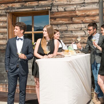 Il tavolo pieghevole "StandUp" è coperto da una tovaglia. Il cameriere serve i quattro ospiti vestiti in modo elegante.
