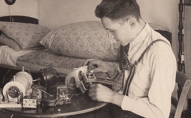 Ein altes Foto von Franz Zingerle. Er sitzt auf einem Stuhl und repariert eine Nähmaschine.