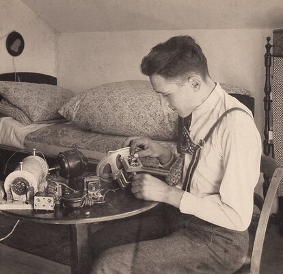 An old picture of Franz Zingerle. He is sitting on a chair while repairing a sewing machine. 