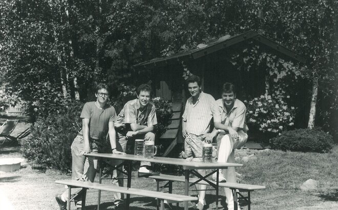 Quattro uomini stanno intorno ad un set da birreria e quattro boccali di birra sono sul tavolo.