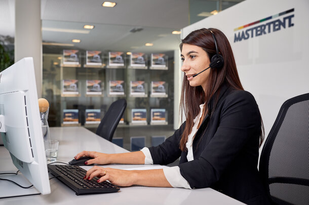 Eine Mitarbeiterin sitzt mit einem Headset vor dem PC und betreut den Kunden am Telefon.