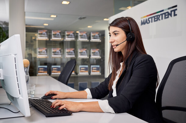 The employee is sitting with her head set in front of the computer while speaking to a client at the phone. 