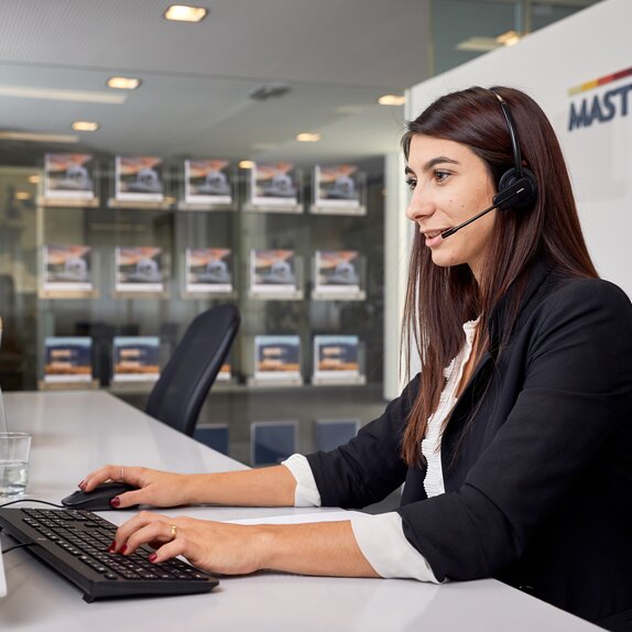 The employee is sitting with her head set in front of the computer while speaking to a client at the phone. 