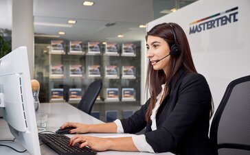 The employee is sitting with her head set in front of the computer while speaking to a client at the phone. 