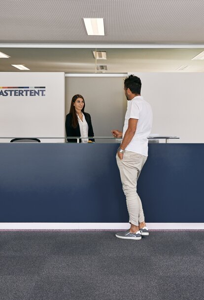 Die Rezeptionistin empfängt den Kunden im Eingangsbereich des MASTERTENT Headquarters.