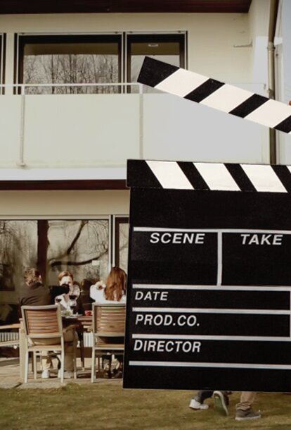 A hand is holding the flap in front of the video scene. Behind it a man is grilling.