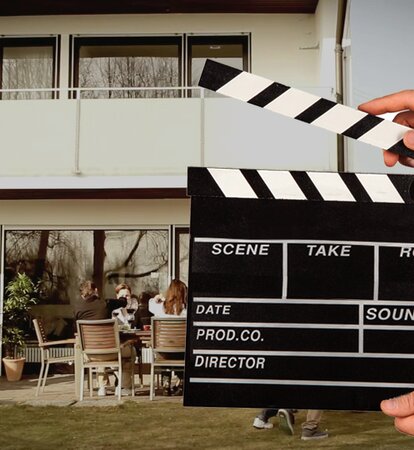 A hand is holding the flap in front of the video scene. Behind it a man is grilling.