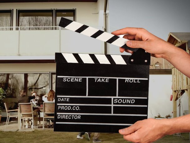 A hand is holding the flap in front of the video scene. Behind it a man is grilling.