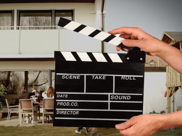 A hand is holding the flap in front of the video scene. Behind it a man is grilling.