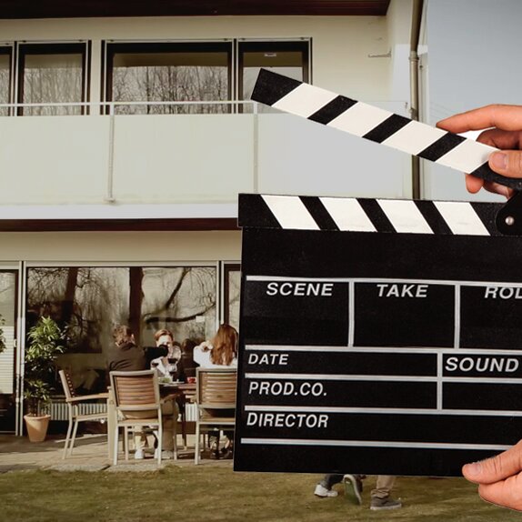 A hand is holding the flap in front of the video scene. Behind it a man is grilling.