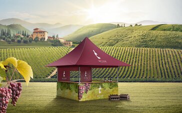 Roter Faltpavillon mit 4 Vordächern steht inmitten der Weinreben. Die Seitenwände sind mit Weinreben bedruckt. Vor dem Zelt stehen 2 Kisten mit Weinflaschen.